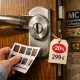 Macro de un cilindro de acero en una puerta de roble; mano compara ofertas: "Encuentra las mejores ofertas en puertas blindadas para instalar en Barcelona".